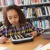 Billede af pige på biblioteket der læser med sin Victor Reader Stratus 12M
